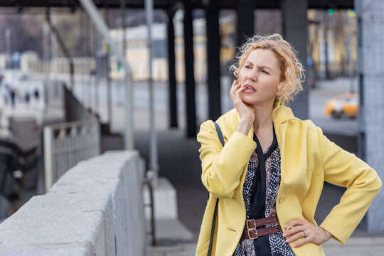 Concerned woman in yellow coat touching face and thinking about problem in city environment