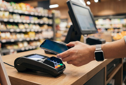 Mobile wallet tap to pay at a supermarket checkout in an everyday retail setting. The image emphasizes a cashless purchase with the phone held above the reader.