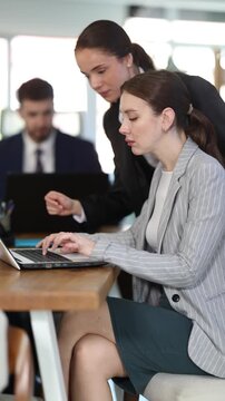 Professional woman helps an intern worker with work on a laptop, they discuss the budget and bookkeeping. Women working together in a modern office