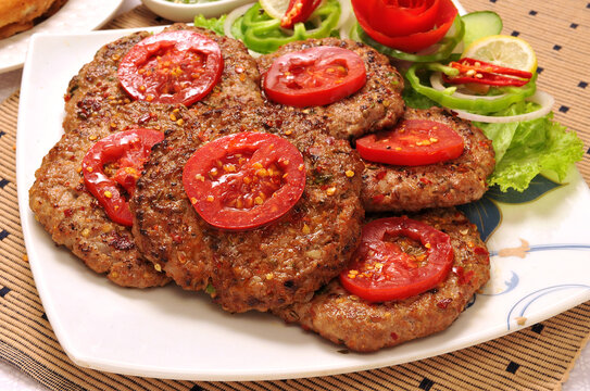 Peshawari Chapli Kabab desi food served with tomato slices and fresh salad on a white plate