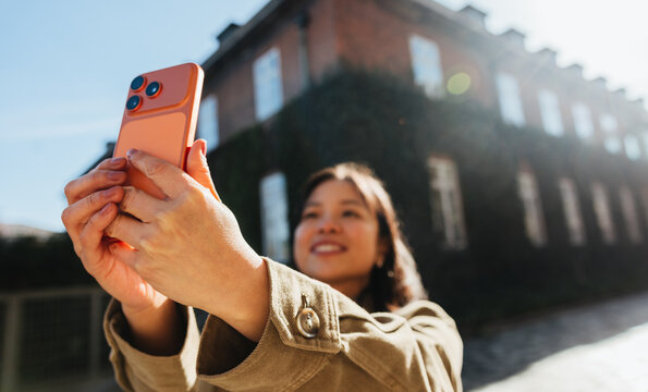 Woman taking a selfie with smartphone outdoors by building