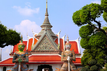 Fototapeta premium Two Colorful Giant Yaksha statues, guarding the entrance of Buddhist Temple of Dawn Wat Arun, sightseeing landmark of Bangkok, Thailand. Topic of summer vacation, relaxing, travel, trip, cruises, tour