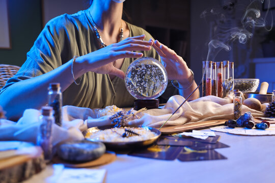 Female fortune teller with crystal ball reading future at table in room