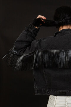 Woman wearing dark grey denim jacket with fringed leather back panel.