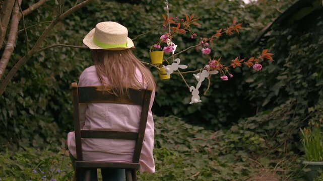Woman wearing Easter bonnet and sits by easter decorations on blossom tree