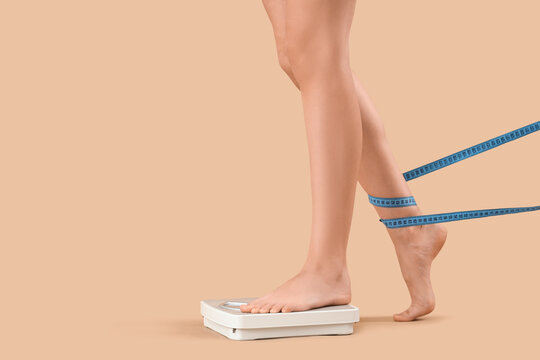 Woman's legs with tape measure and weight scales on beige background. Anorexia concept
