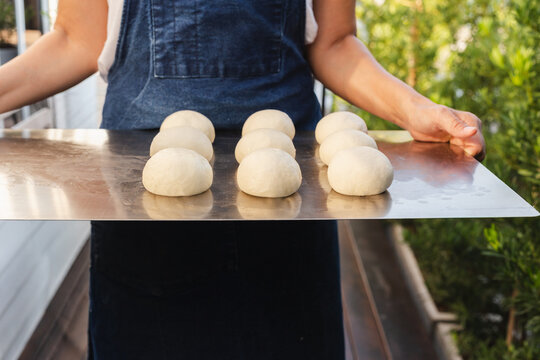 Baker holding a metal tray with fresh raw dough balls prepared for baking.