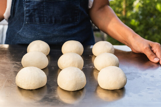 Baker holding a metal tray with fresh raw dough balls prepared for baking.