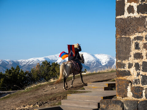 Man on horse in traditional Caucasus hat carrying flag of Armenia and Artsakh (Nagorno-Karabakh) outside of Sevanavank Monastery, Geghardkunik Province, Armenia with mountains in the background