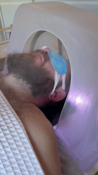 Bearded Man with Blue Eye Patches Lying Inside Japanese Head Spa Bowl with Purple UV LED Illumination, Luxury Scalp Steaming and Chromotherapy Ritual in Premium Beauty Salon, Male Wellness Treatment 