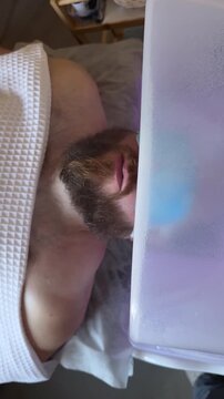 Bearded Man with Blue Eye Patches Lying Inside Japanese Head Spa Bowl with Purple UV LED Illumination, Luxury Scalp Steaming and Chromotherapy Ritual in Premium Beauty Salon, Male Wellness Treatment 