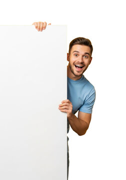 Young caucasian man in light blue t-shirt excitedly peeking over a transparent vertical copy space sign, brightly illuminated on a vibrant yellow studio background. Concept for promotional surprise