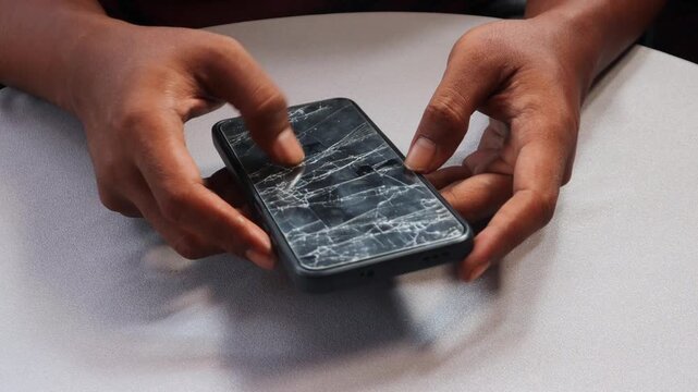 Close up of Asian male hand holding a smartphone with severely cracked screen, broken glass from drop damage, gadget repair concept and damaged technology.