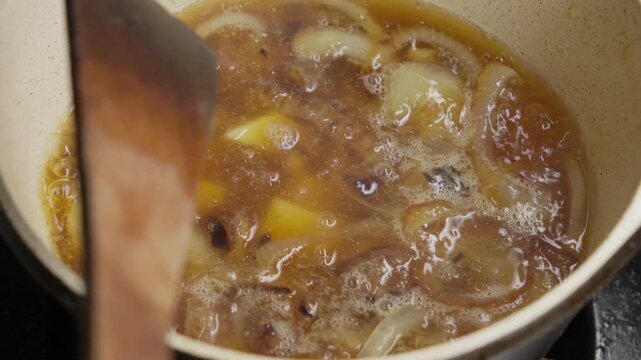 Slow motion close up of a fresh potato slice falling into a boiling vegetable stew. This nutritious meal is being cooked in a modern kitchen in a residential home