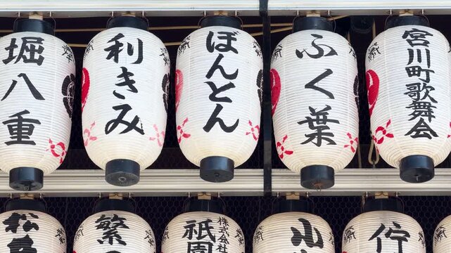 Rows of traditional Japanese paper lanterns with black calligraphy hanging outdoors.
