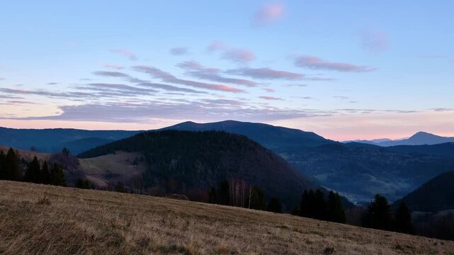 Dusk timelapse of a mountain landscape with rolling hills and a clear blue sky.