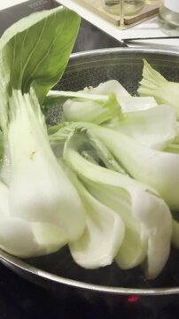 fresh bok choy cooking in a pan with steam rising; leafy Asian greens are being gently saut&eacute;ed; a healthy vegetable cooking process in a home kitchen