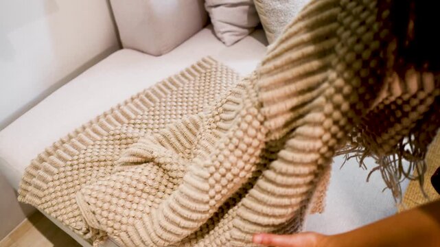 Person unfolding a textured knit throw blanket on a neutral couch in a modern living room setting.