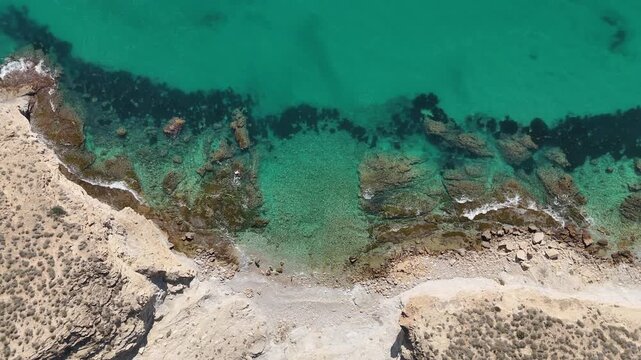 Drone ascending top down over rocky beach with clear Mediterranean seabed