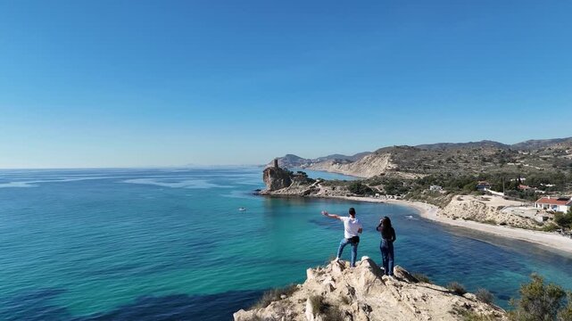 Low drone flight over couple looking at ruined coastal tower on cliff
