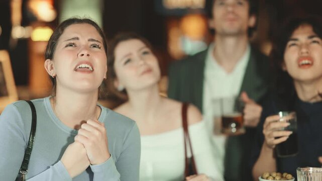 Sports fans react with disappointment to changes in bad luck game. Group of friends hangs out at sports bar, watching teams match, and following progress of game. Video broadcast of match or race is