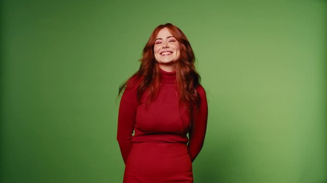 Happy woman in red smiles, winks, and laughs on green screen background. Studio portrait, medium shot, slow motion.
