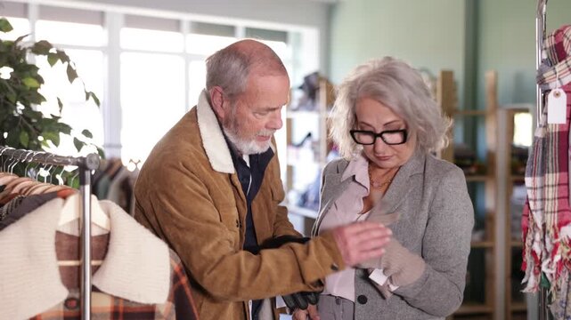  Mature couple spend time in shop and choose wool gloves. Changing wardrobe, shaping style of clothing. Designer clothes, clothing of world brands