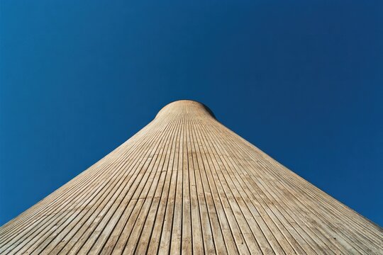 A striking low-angle perspective captures the unique, curved architecture of a modern building against a vibrant, clear blue sky, emphasizing its geometric design and scale.
