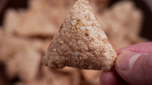 Dietary organic buckwheat nacho in male hand. Triangular brown cracker.