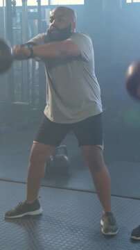 Vertical video: Gripping kettlebell, man driving hips and swinging at gym, training in gray tee