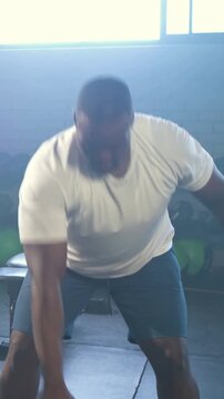 Vertical video: Bending to grab kettlebell, man in white tee training single-arm swings at gym
