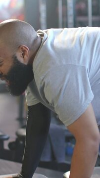 Vertical video: Gripping hex dumbbell, man rowing on bench at gym for strength, compression sleeve