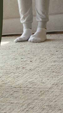Vertical video: Gripping corner, man unrolling green mat onto carpet near sofa for yoga in socks