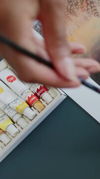 Vertical video: Entering frame, woman arranging brushes on tabletop, preparing boxed oil tubes