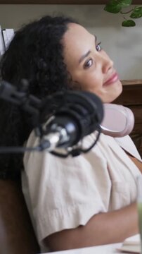 Vertical video: Speaking host with pink headphones leaning into mic home by green drink recording