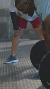 Vertical video: Clapping spotter cueing lifter bracing for loaded barbell at gym, red shorts