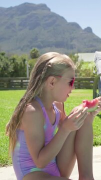 Girl sitting pool lifting watermelon and biting causing animated juice drops for family lifestyle