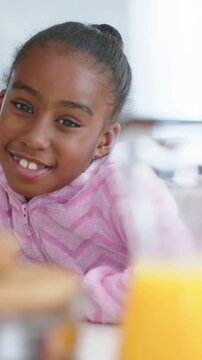 Vertical video: Smiling girl in pink zipup reacting to camera starting at table, jar, orange bottle