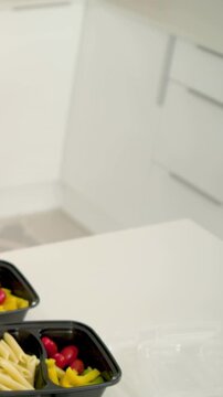 Vertical video: Reaching toward pink bowl hands adding tomatoes into boxes for meal prep, watch