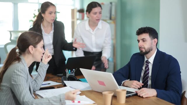 Group of women scold young man while he sits looking sad in office