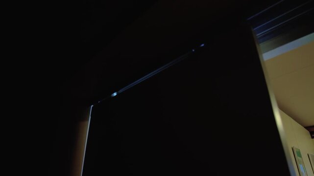 Firstperson view screwing cabinet guide inside dim kitchen cabinet, installer tightening metal drawer slide with screwdriver, closeup of hand and screw, warm doorway light casting