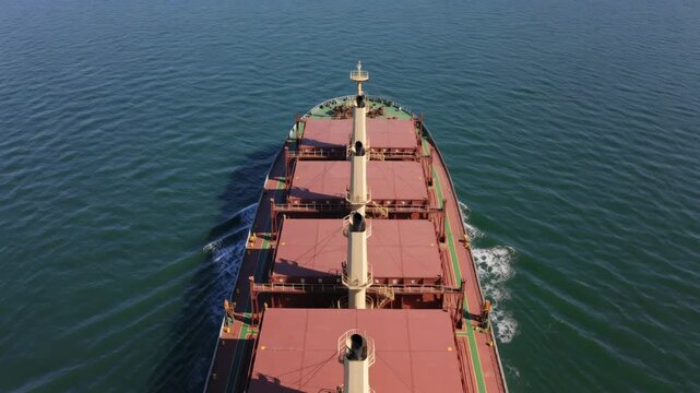 Powering bulk cargo ship moving forward through calm open sea, with red hatch covers