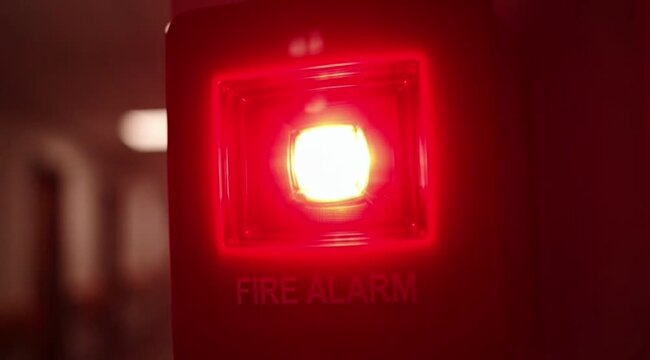 Close-up of a red fire alarm strobe flashing in a hallway, signaling danger with urgent light.