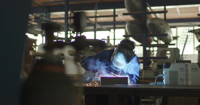 Welder working at a bench in an industrial workshop with sparks flying during the process