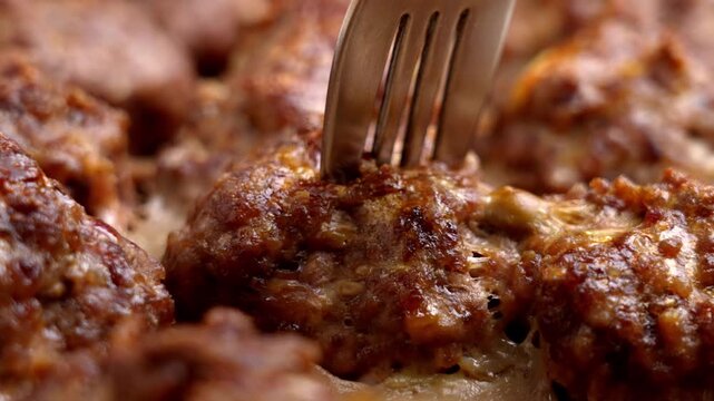Metal fork piercing a juicy roasted meatball close up