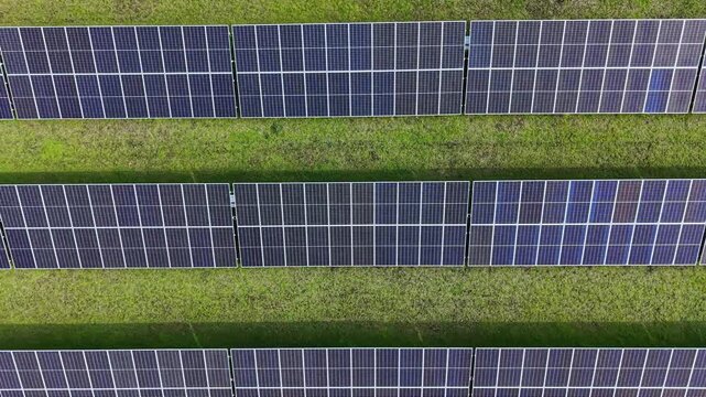 Rows of solar panels are placed on a grassy area. The sun shines brightly above, showing a clean and modern setup for energy production in operation.