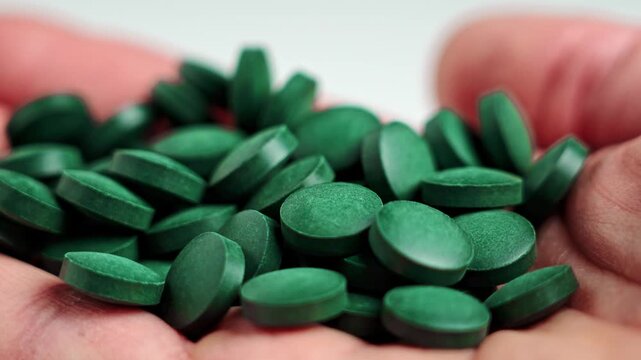 Green spirulina tablets held in human hand. Close up of natural dietary supplement rich in nutrients. Organic algae pills. Detox and plant based nutrition concept