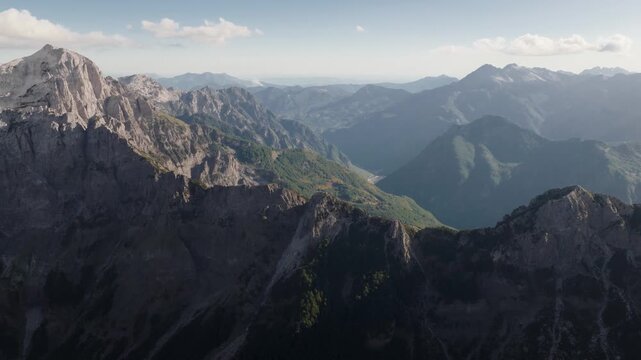 Aerial view of rugged, grey mountains and lush green valleys under a soft sky, creating a dramatic contrast of textures and tones, Teth, Shkoder County, Albania.