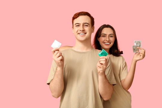 Young couple with condoms on pink background. Safe sex concept