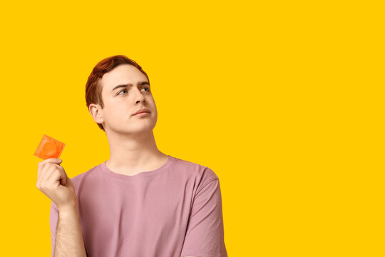 Thoughtful young man with condom on yellow background. Safe sex concept